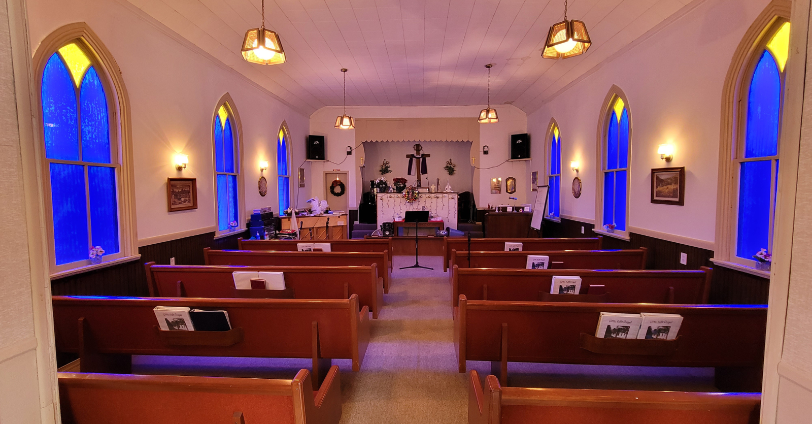 Interior of Little Falls Chapel with rows of pews, arched windows, and a decorated altar, bathed in warm light.