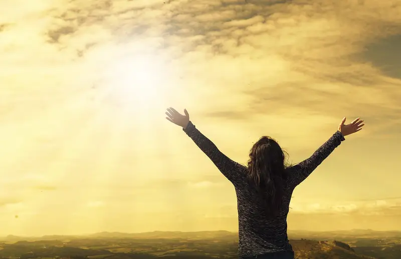 A person with arms raised towards the sky in an expression of worship, with a beautiful golden sky in the background.