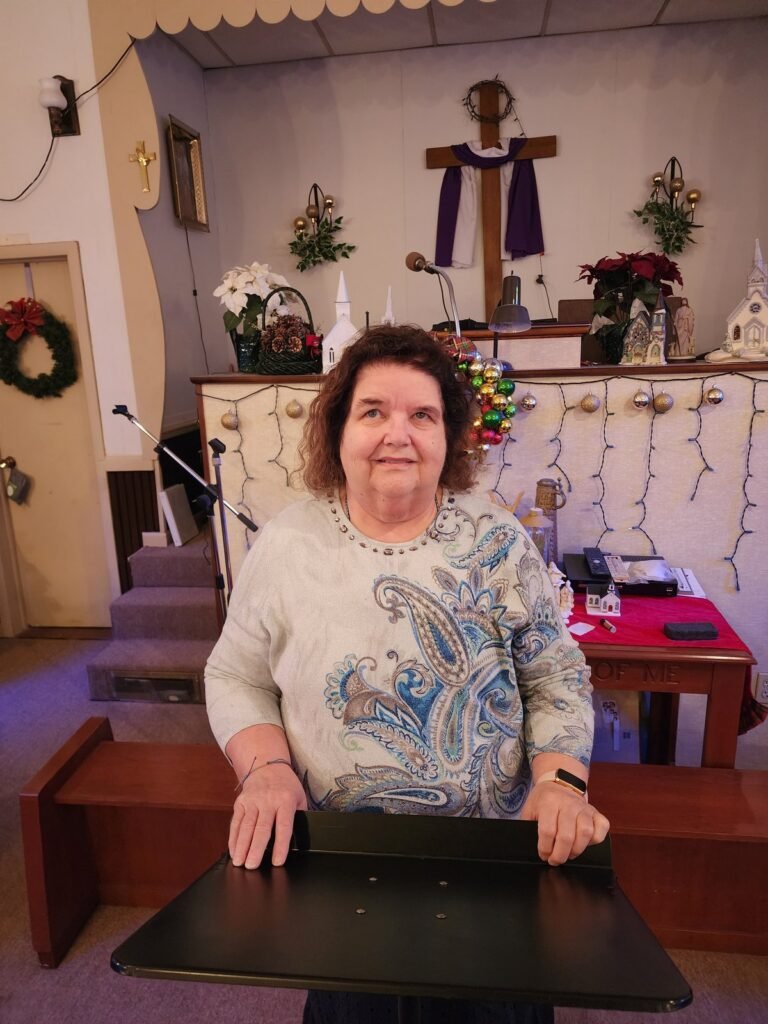 Pastor Linda Reese of Little Falls Chapel, smiling, at the front of the chapel